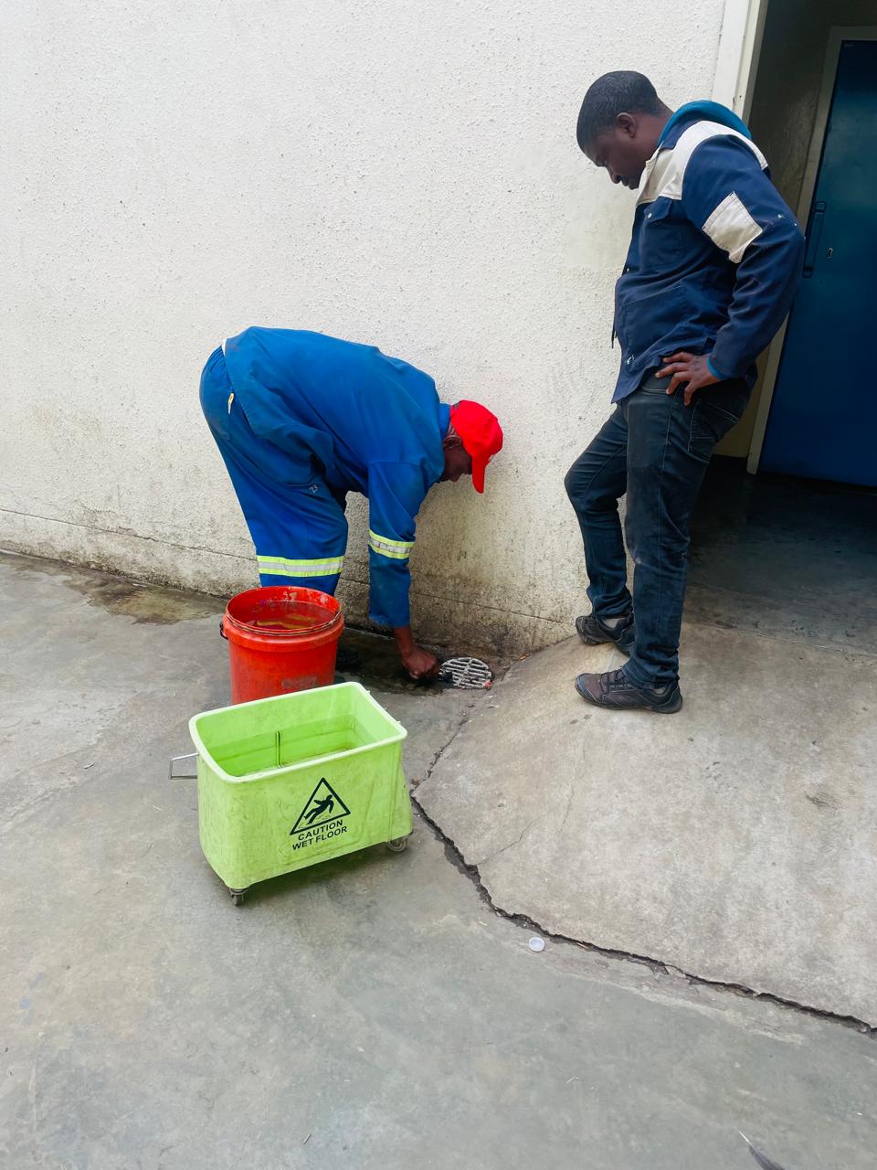 Workers servicing an exterior drain beside a building entrance